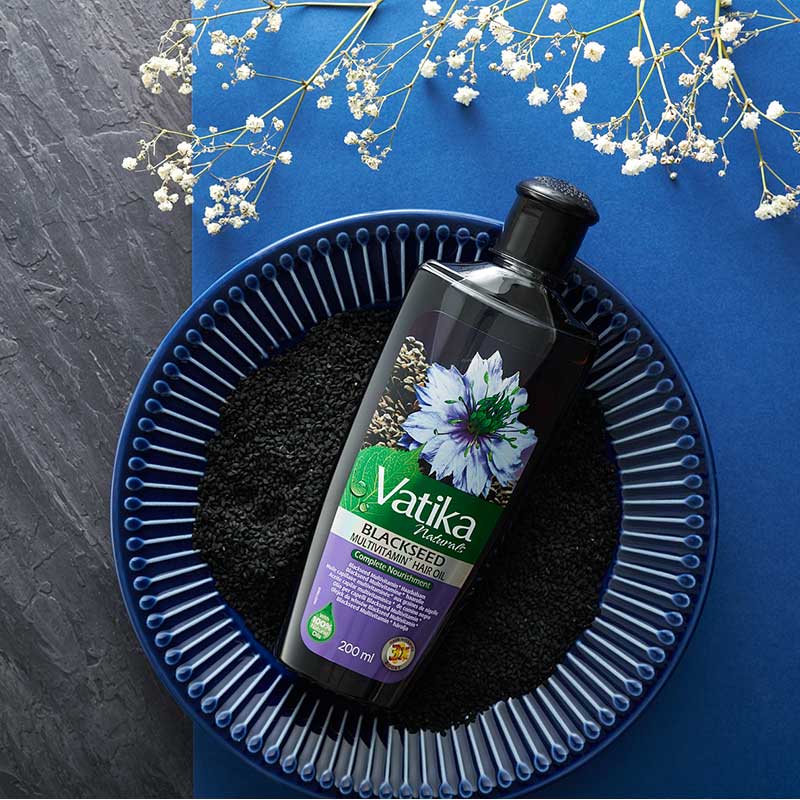 Vatika Blackseed hair care product on a blue plate with flowers on a blue background