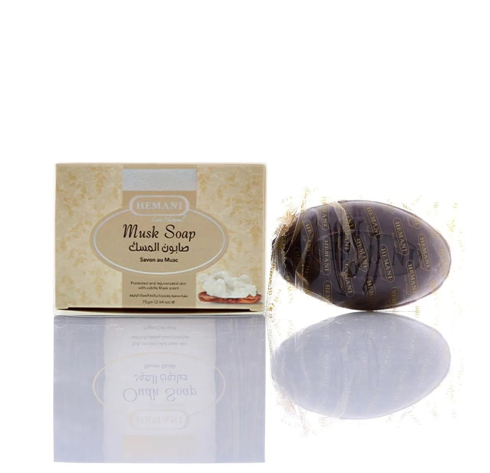 Hemani Musk Soap shown with its beige patterned retail box and a dark brown oval-shaped wrapped soap bar on a white reflective surface.