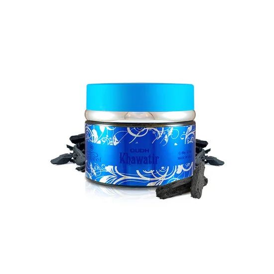 A small cylindrical tin of Oudh Khawafir perfume oil with a bright blue lid and a blue label decorated with white floral patterns. The tin is displayed on a white background with dried black cardamom pods scattered around its base.