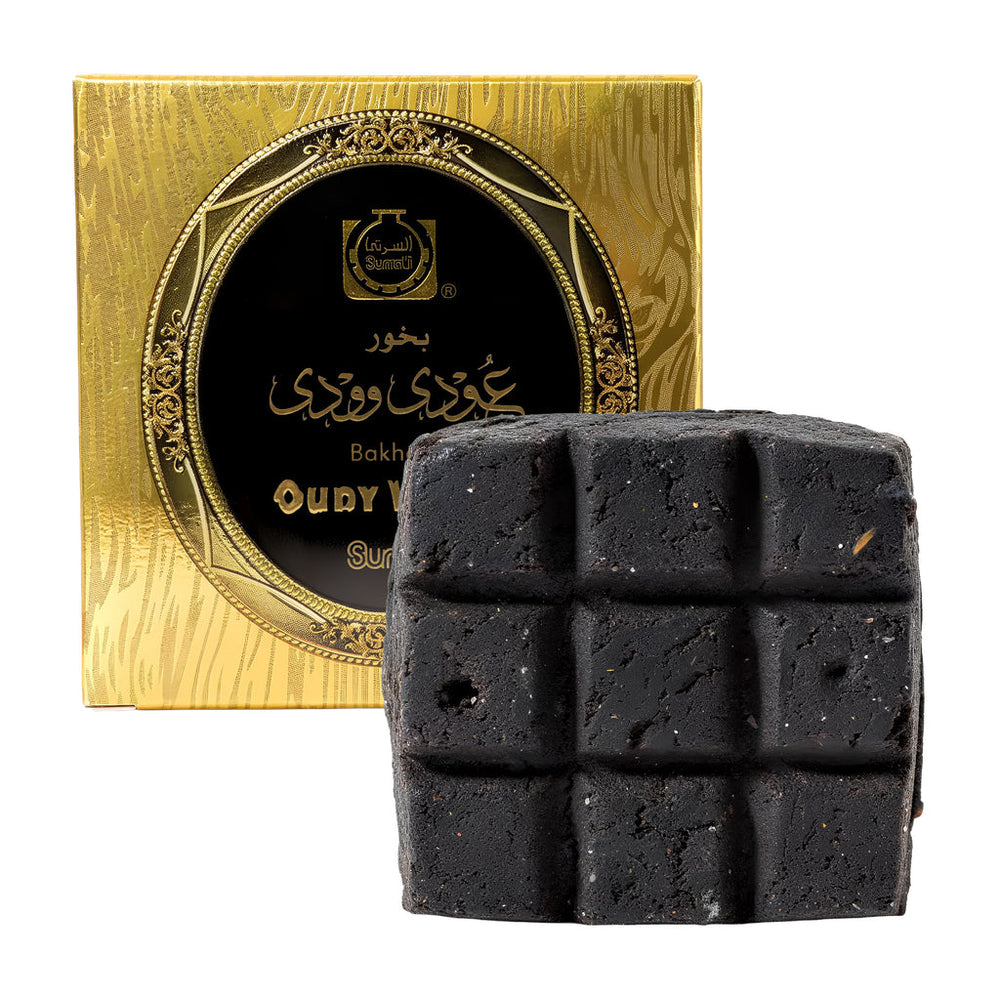 A dark charcoal-colored baked bar with a grid pattern, shown in front of its ornate gold and black packaging box on a white background.Oudy Woody Choco Bakhoor 40g – Surrati