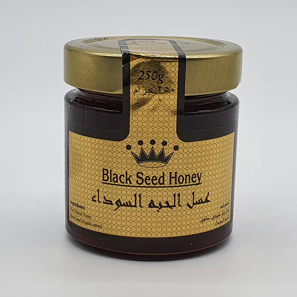 A jar of Black Seed Honey with a gold lid and a gold honeycomb-patterned label featuring a crown logo and Arabic text, set against a plain light gray background.