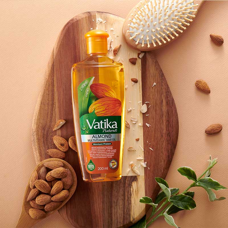 Vatika Almond hair oil bottle on a wooden board with almonds and a plant