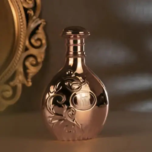 A rose gold metallic perfume bottle with floral engravings and slender neck for arabiyat prestige nyla edp fresh citrus fragrance