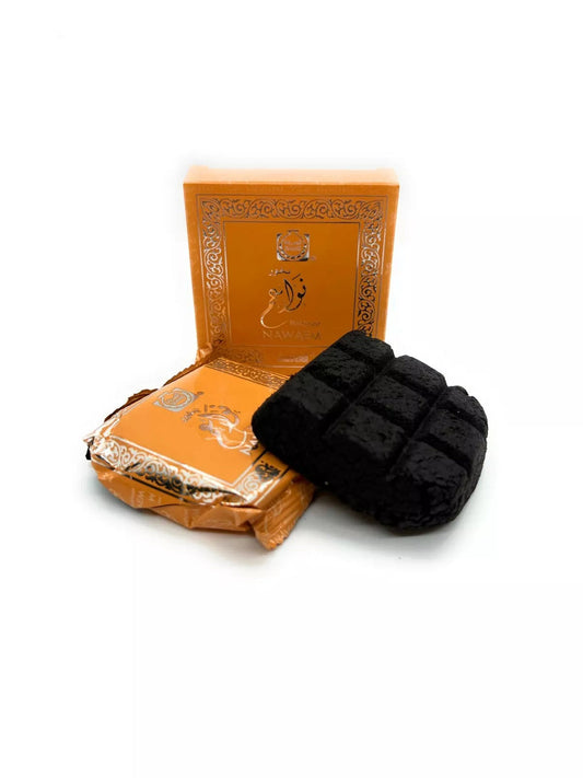 A black textured charcoal plug with a square grid pattern, displayed next to its orange and gold decorative packaging box on a white background.Bukhoor Nawaem 40g – Surrati