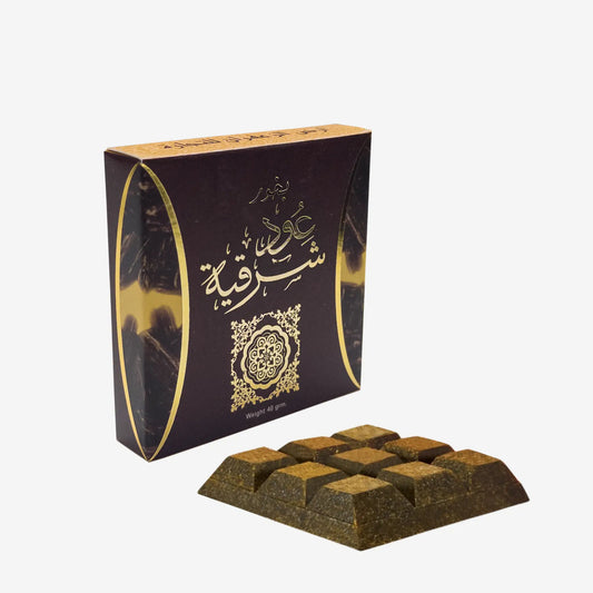 A boxed dark brown chocolate bar set with Arabic calligraphy on the packaging, shown on a plain light gray background. One chocolate bar is placed in front of the box.