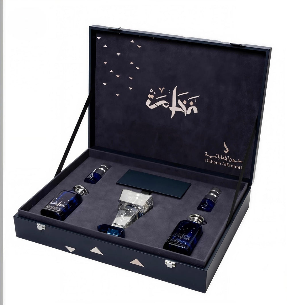 An open dark blue presentation box containing a set of perfume bottles and a rectangular box, photographed on a plain white background. The inside lid has Arabic calligraphy and branding text.Al Fakhama Luxury Fragrance Gift Set 6 Pieces – Dkhoon AlEmiratia