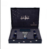 An open luxury presentation box containing three dark blue glass bottles and a clear glass decanter, set against a plain white background. The box is dark navy blue velvet with silver metal latches and geometric accents, featuring Arabic calligraphy and the brand name 'Dehshan Al-Mushatta' printed on the inside lid.Al Fakhama Luxury Fragrance Gift Set 6 Pieces – Dkhoon AlEmiratia