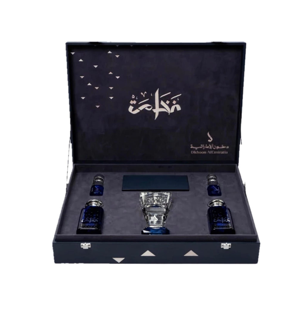 An open dark blue presentation box containing a clear faceted glass vessel in the center and two small dark blue bottles on either side, photographed on a plain white background.Al Fakhama Luxury Fragrance Gift Set 6 Pieces – Dkhoon AlEmiratia