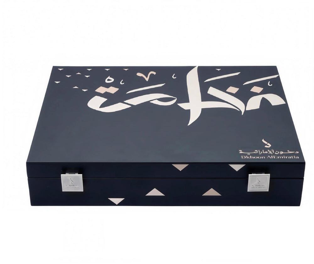A dark navy blue rectangular presentation box with silver-tone metal latches, featuring white Arabic calligraphy and small geometric triangle accents on the lid, photographed on a plain white background.Al Fakhama Luxury Fragrance Gift Set 6 Pieces – Dkhoon AlEmiratia