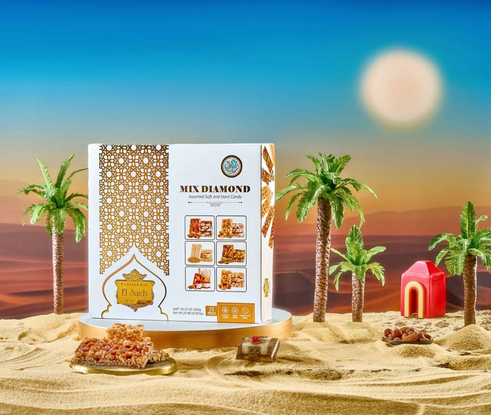 A boxed food product labeled 'MIX DIAMOND' stands on a pedestal in a stylized desert scene with sand, palm trees, a sunset sky, and a small red house. The package is white with ornate gold patterning and gold accents, and several pieces of the product are placed in front.