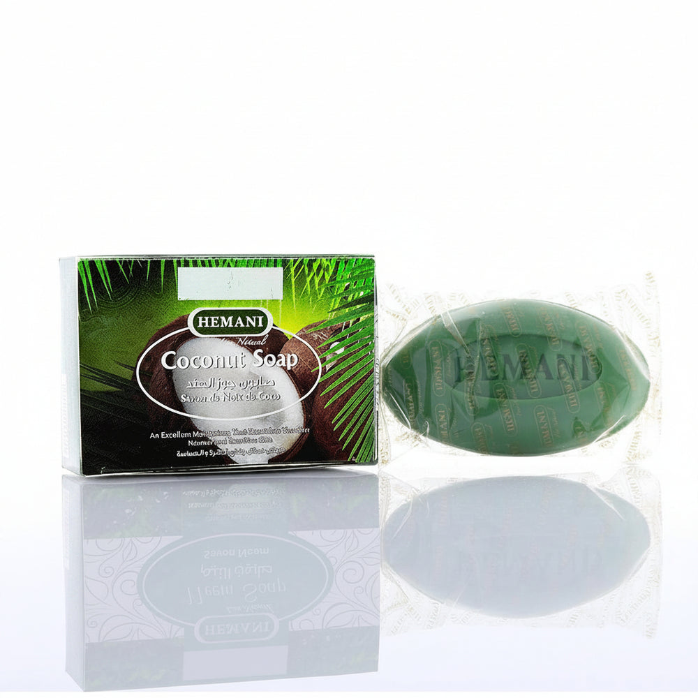 Hemani Coconut Soap shown with its retail box on a reflective white surface. The soap bar is green and wrapped in clear foil, and the box features coconut and palm leaf graphics with the Hemani brand name.
