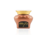 A glass jar of Maamul Wardi perfume oil with a metallic rose gold body, a gold cap, and a black label with gold lettering, set against a plain white background with a soft reflection.Maamul Wardi Oud Muattar Bakhoor 48g – Khadlaj