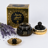 Mamoul Kuwati black charcoal face mask set, featuring a black and gold patterned box, a jar of dark charcoal mask, a gold dish with black mask balls, and a small gold dish with a single black mask ball, styled with lavender sprigs on a white background. Mamoul Kuwaiti Bakhoor 60g – Gulf Incense