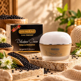 Hemani Blackseed Cream 50g jar and packaging box displayed on a stone slab with black seeds, flowers, and green leaves in a warm, natural setting.
