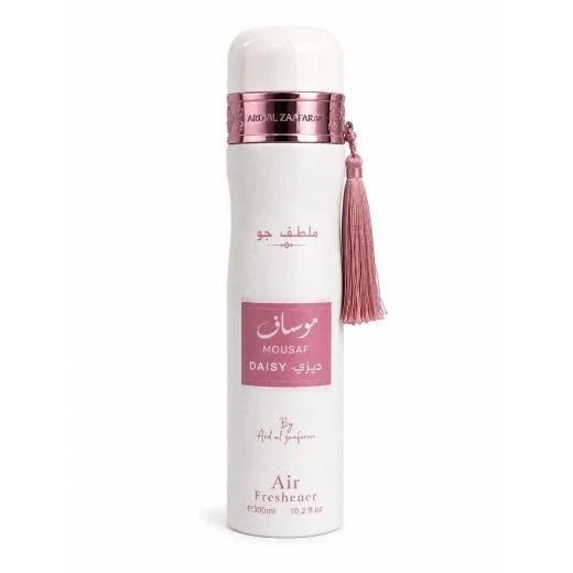 A white cylindrical air freshener bottle with a pink metallic collar, a pink tassel, and pink and black text on a white background. The brand name 'By Ariel perfume' is visible near the bottom. Mousuf Daisy  Mousuf Daisy 300ml Air Freshener – Ard Al Zaafaran