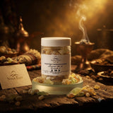 A clear jar of Noor East Omen Holiq Frankincense (Bubal) incense sticks sits on a glowing white dish on a rustic wooden table. The scene is warmly lit with golden light and steam rising in the background, with scattered incense pieces and a branded card in the foreground.