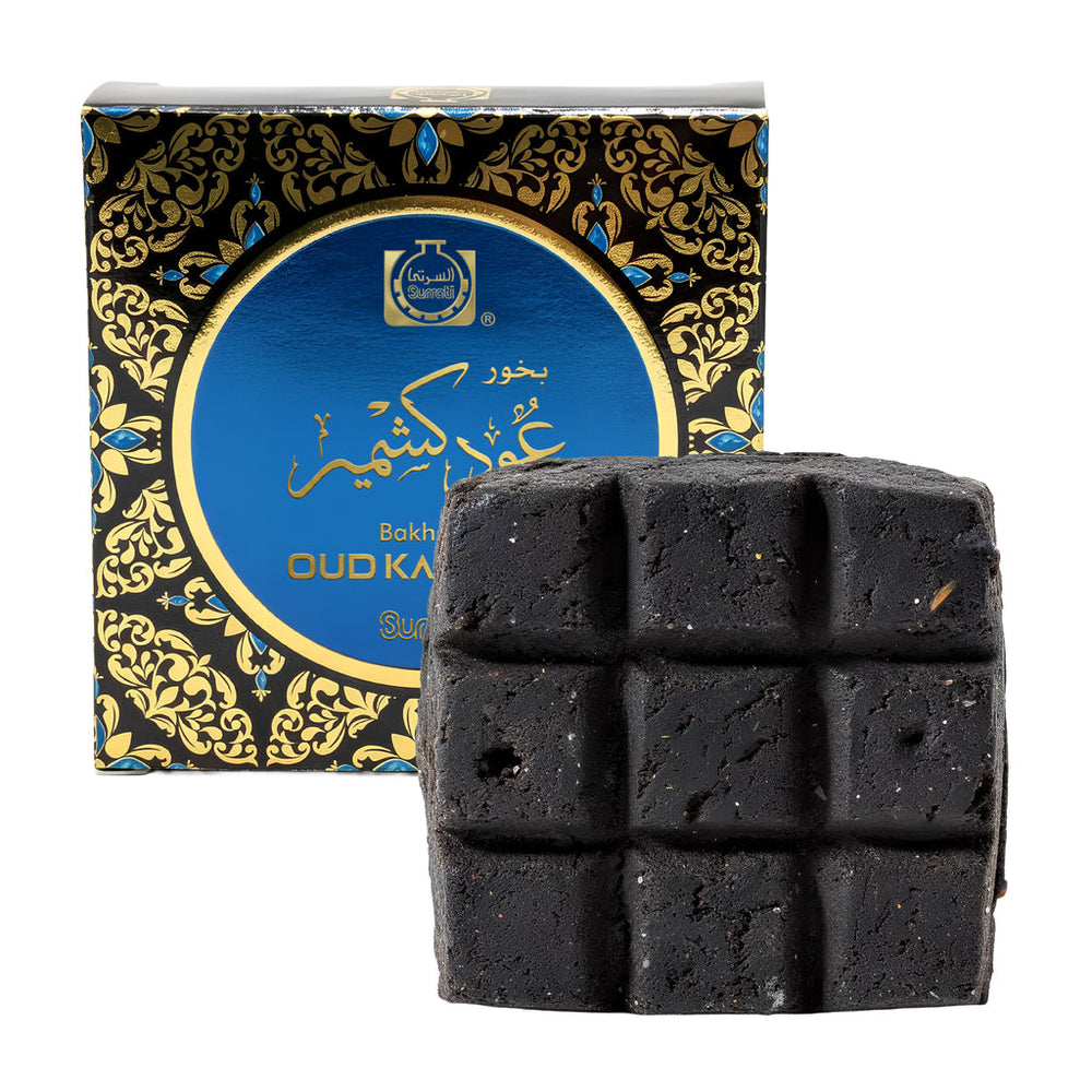 A square dark charcoal-colored soap bar with a 3x3 grid texture, shown in front of its ornate black and blue packaging box with gold details. The box features a prominent blue circular label with gold lettering.