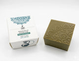 Green soap bar with embossed design next to its packaging on a white background