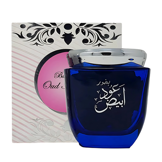 A cobalt blue glass perfume bottle with Arabic calligraphy on the front, shown in front of its white and pink patterned box packaging.Oudh Abiyedh Bakhoor 80g – Ard Al Zaafaran