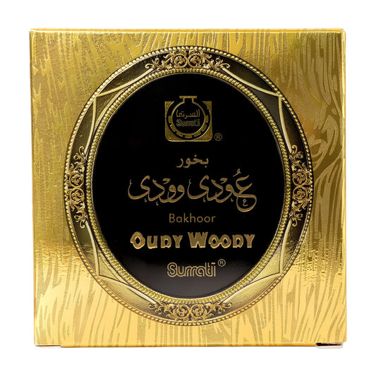 A close-up of a round gold-toned product package with a black circular label reading 'Golden Hour' and 'Super Oudy Woody Choco Bakhoor 40g – SurratiMoist'.