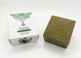Green soap bar with decorative patterns next to its packaging on a white background