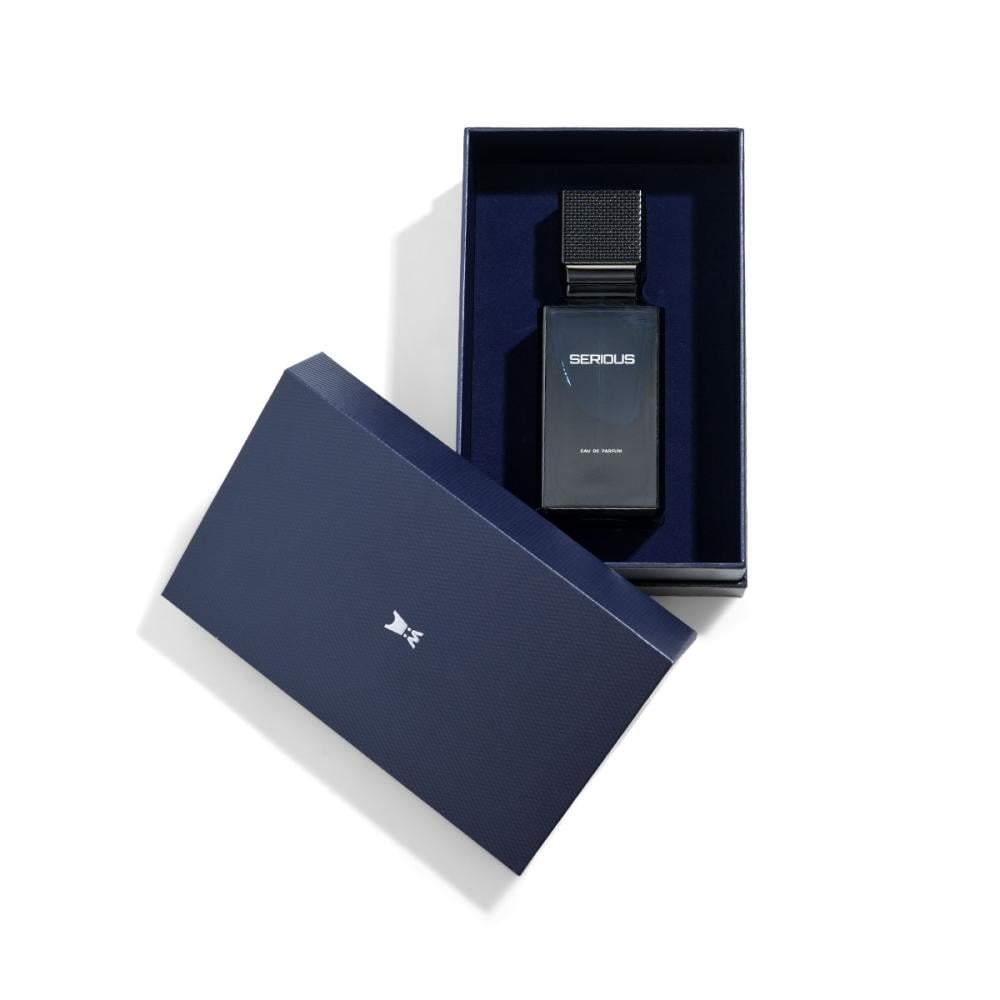 A dark navy blue rectangular perfume bottle labeled 'SERIOUS' displayed inside an open matching navy box, with the lid placed beside it on a clean white background.Serious – Amber Fougère EDP 100ml – Al Majed Oud