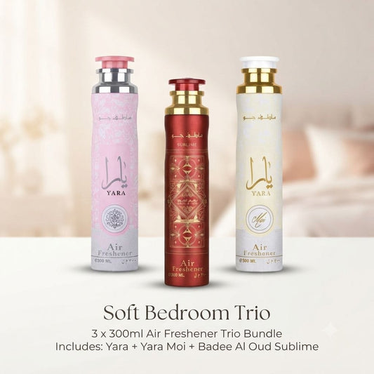 Three air freshener bottles in a Soft Bedroom Trio bundle are displayed against a warm, softly blurred bedroom background. The set includes a pink bottle labeled Yara, a metallic red bottle labeled Yara Moi, and a cream bottle labeled Badede Al Oud Sublime, with text below describing the bundle.