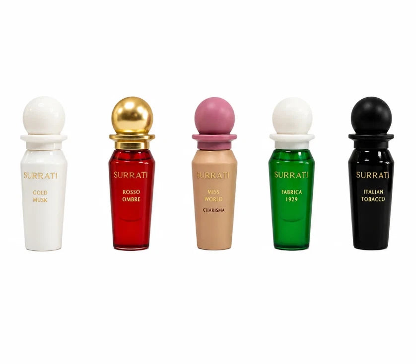 Five Surrati perfume bottles in different colors are lined up on a white background: white Gold Mola, red Rosso Ombre with a gold cap, beige Rossa Umbra with a pink cap, green Fabbrica 1929 with a white cap, and black Italian Tobacco.