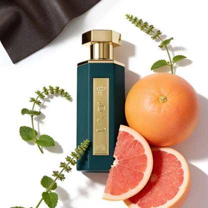 Perfume bottle with gold cap and green label next to a grapefruit and its slices on a white background