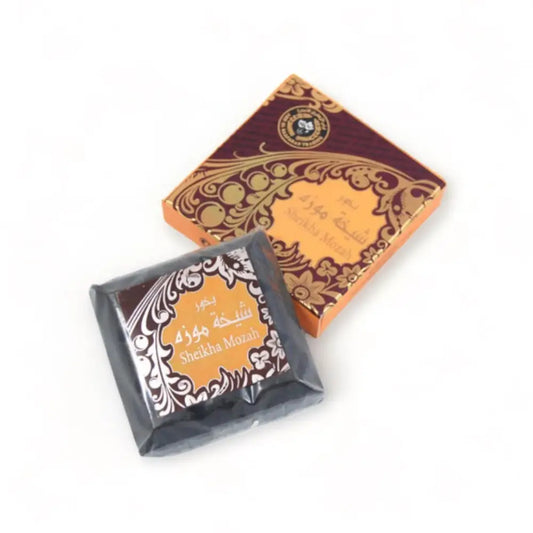 Dark square block of bukhoor sheikha mozah incense wrapped in black foil with white floral patterns by ard al zaafaran