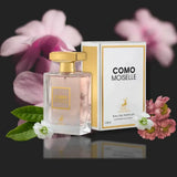 A clear glass perfume bottle with gold cap and light pink liquid beside its white and gold box of como moiselle maison alhambra