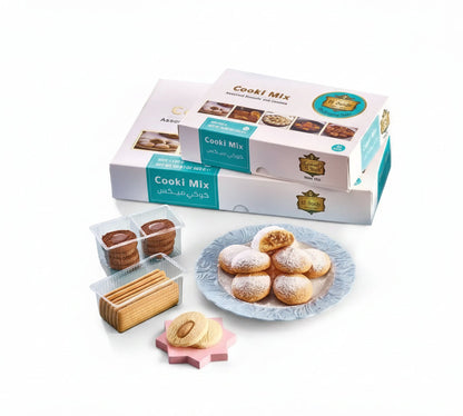 White and teal cooki mix biscuit boxes with gold logos stacked beside clear containers of assorted middle eastern cookies