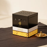 Black and gold cube-shaped electric quran speaker with perforated top, white band, and illuminated golden brick base