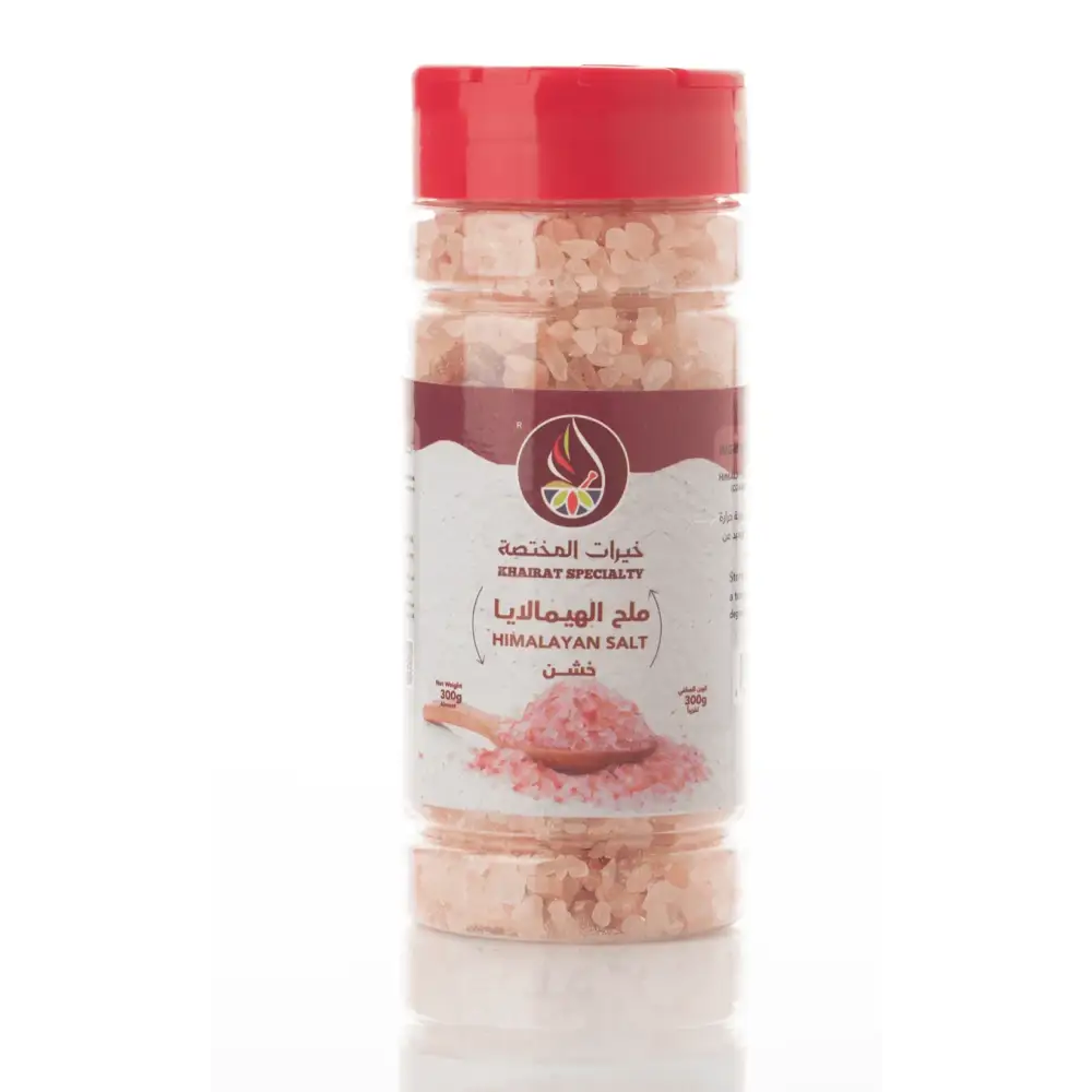 A clear jar with a red lid contains natural himalayan pink salt coarse crystals labeled khairat specialty in arabic and english