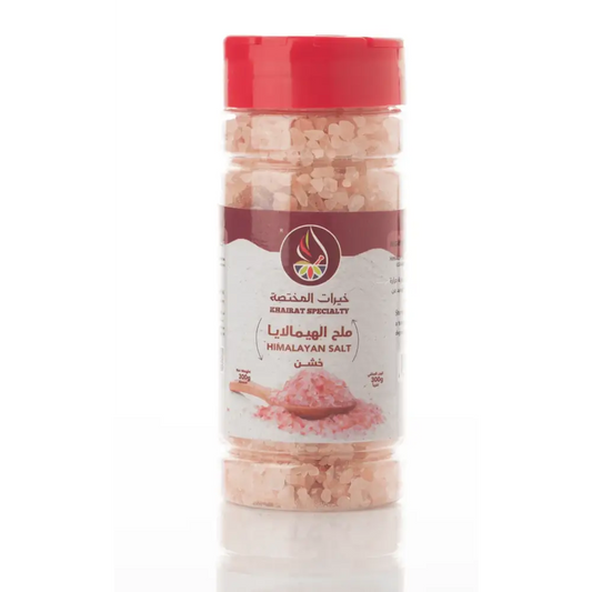 A clear jar with a red lid contains natural himalayan pink salt coarse crystals labeled khairat specialty in arabic and english