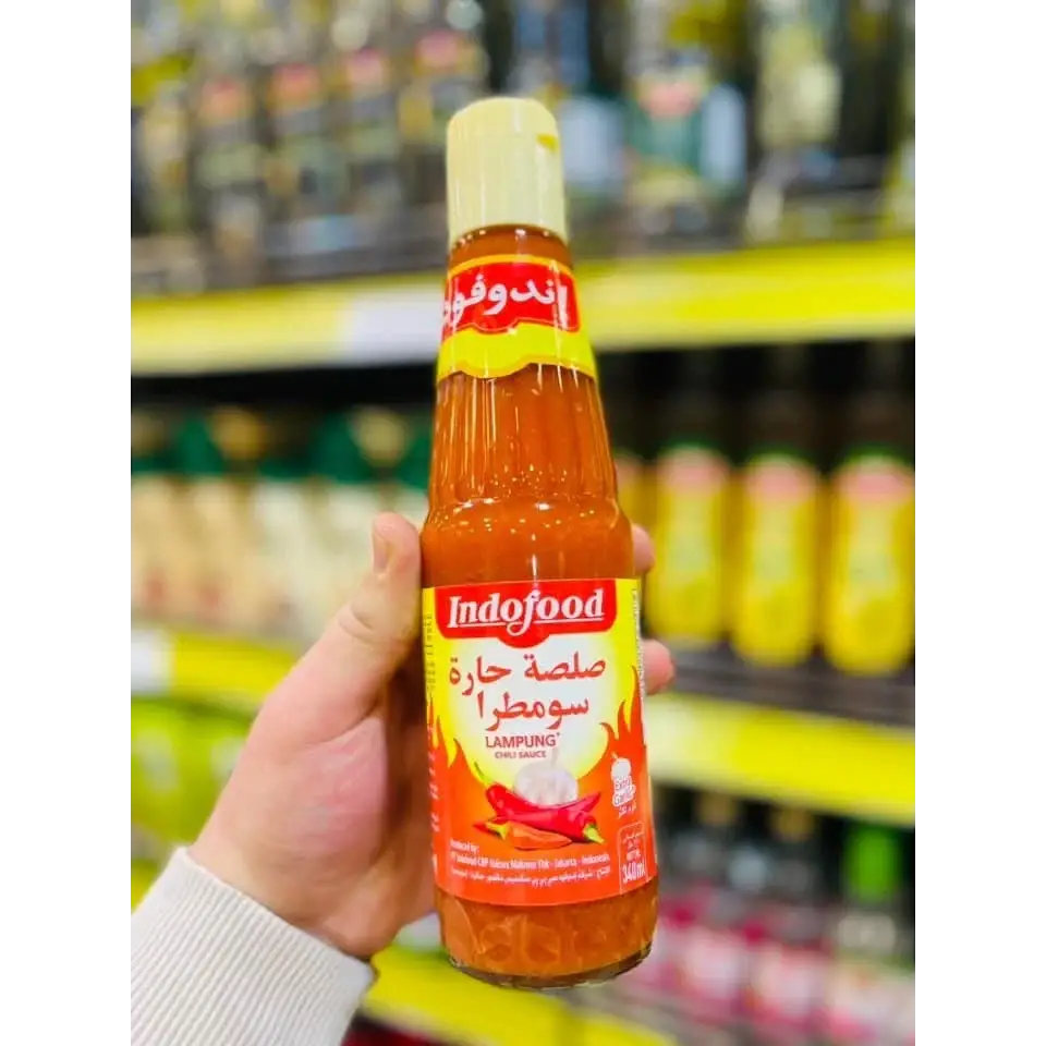 A vibrant orange Indofood hot chili sauce bottle 340ml with a yellow cap and Arabic script on a red label held in hand