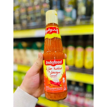 A vibrant orange Indofood hot chili sauce bottle 340ml with a yellow cap and Arabic script on a red label held in hand