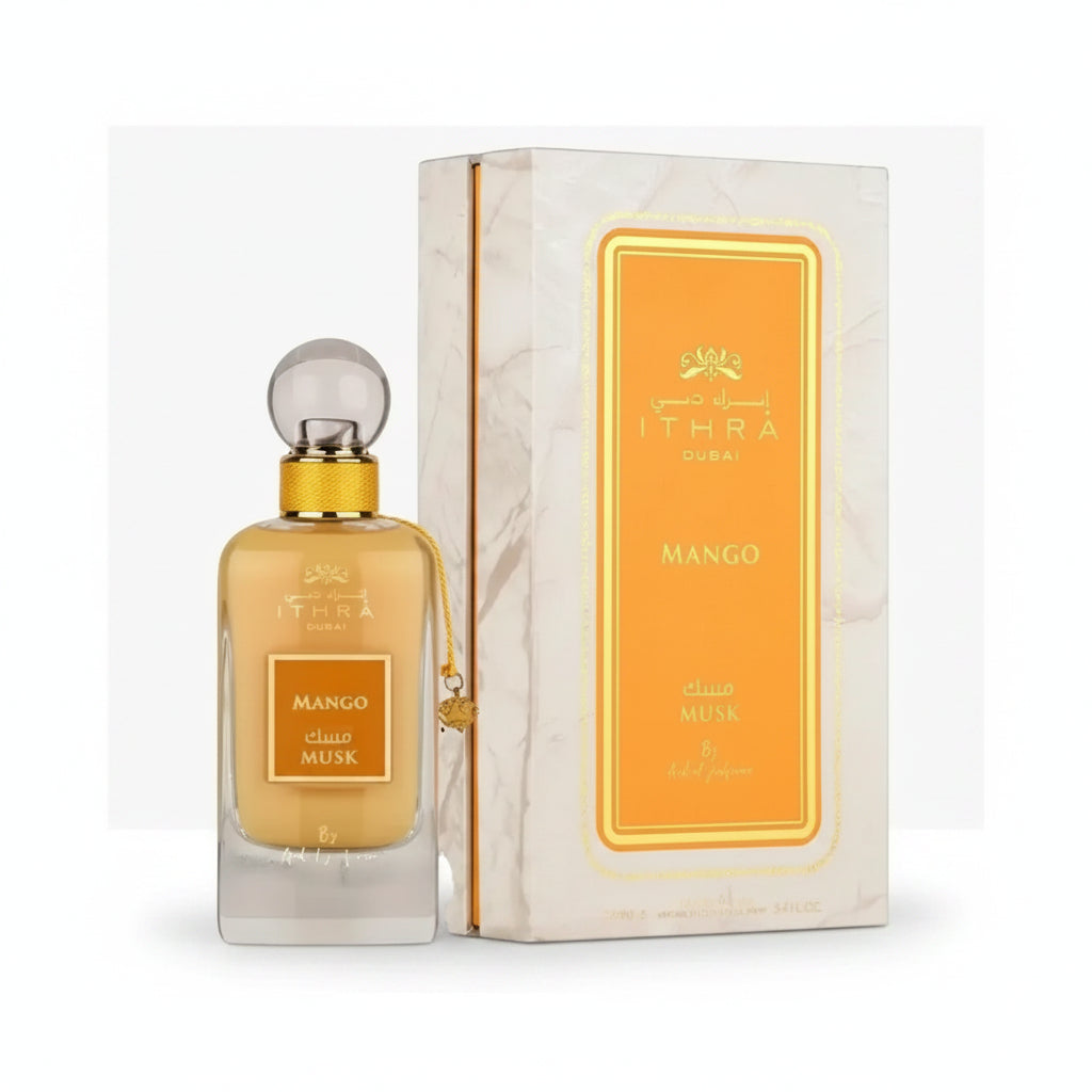 Golden-hued ithra dubai musk mango eau de parfum 100ml in clear glass bottle with gold cap beside marble box