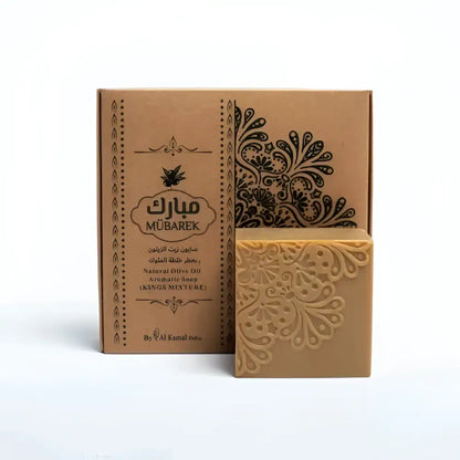 A beige intricately carved Mübarek natural olive oil soap bar with floral pattern beside brown cardboard packaging