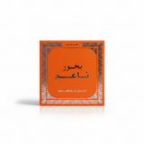 An orange square product box with Arabic text and a decorative white border, placed on a beige woven fabric background.