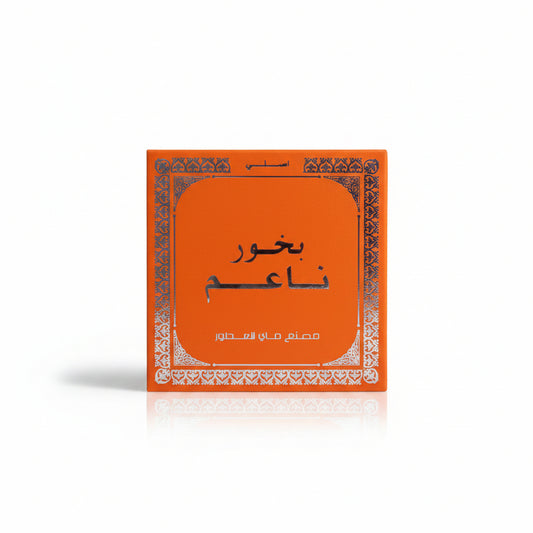 An orange square product box with Arabic text and a decorative white border, placed on a beige woven fabric background.