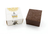 Brown soap bar with decorative patterns next to its packaging on a white background