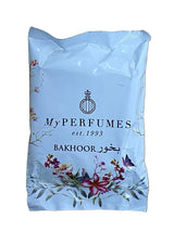 A white plastic pouch of My Perfumes Bakhoor fragrance, featuring black text and floral illustrations, resting on a light brown wooden surface.